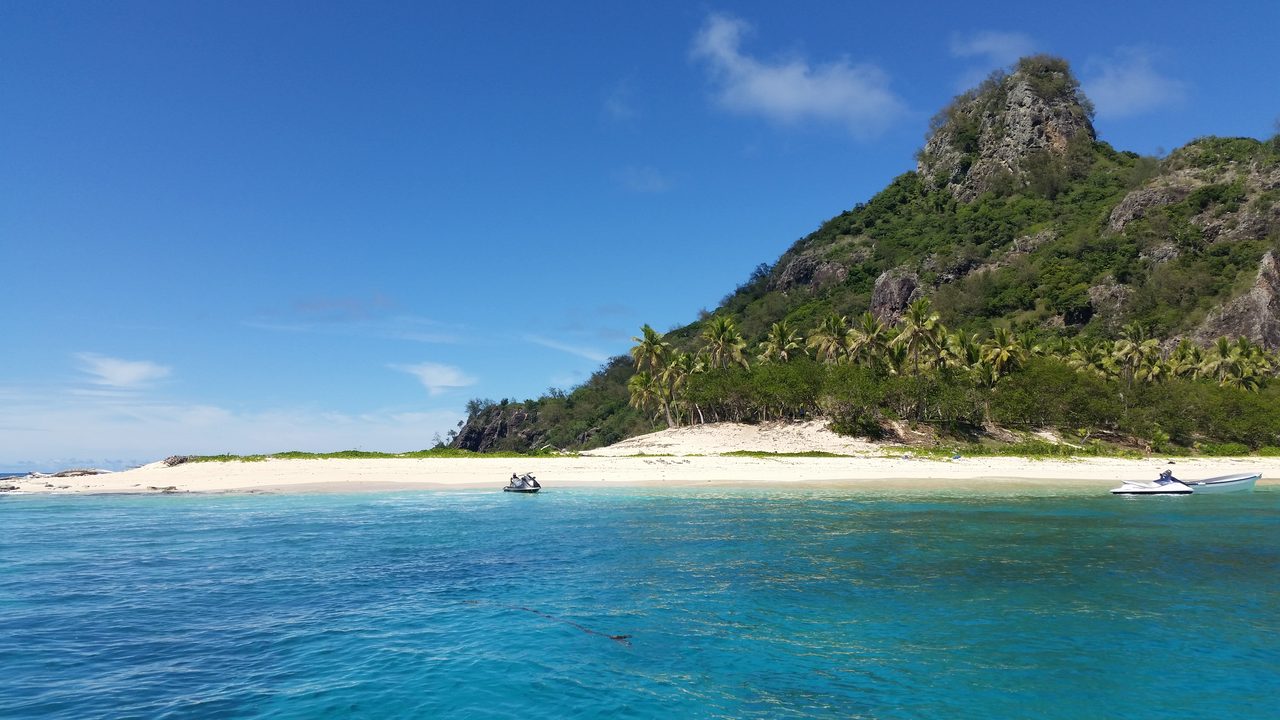 A small white-sand island with palm trees and turquoise water in the Mamanuca Islands, Fiji